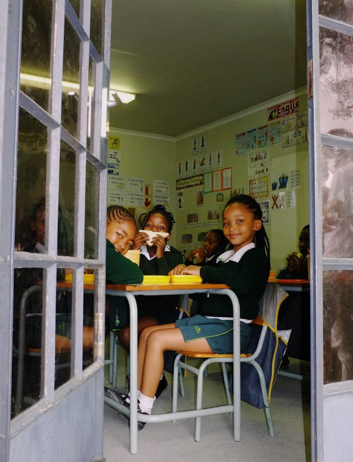 about-us-01 Young students sitting in classroom enjoying lunch, surrounded by educational materials.