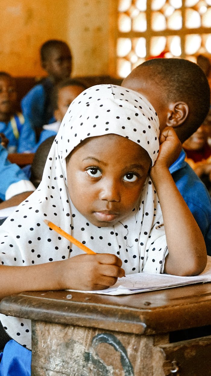 heros-img Young girl focused on writing in a vibrant classroom environment.