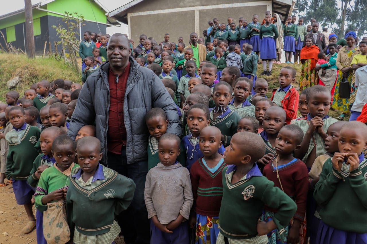 about-us-02 A large group of African children and an adult gather outside a rural school setting, showcasing community spirit.